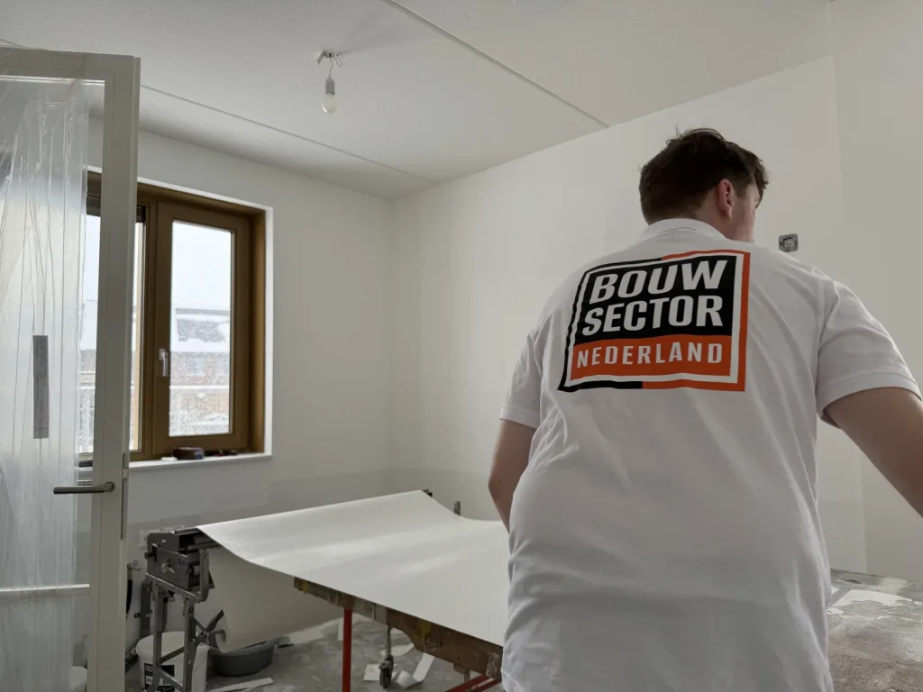 Behanger van Bouwsector Nederland rolt een baan uit over de plaktafel in een kale nieuwe kamer met afgedekte deur