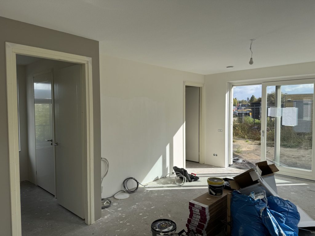 Nieuwe woonkamer tijdens de afwerking, met verfemmers, pakken laminaat en openslaande deuren naar een bouwterrein