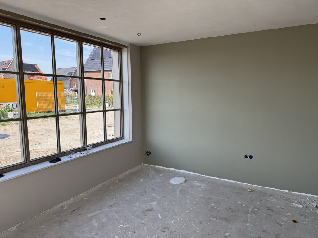 Nieuwbouwkamer met een groot raam met roeden en een egaal afgewerkte wand in een grijsgroene tint