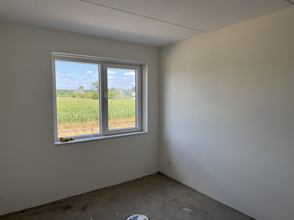 Lege slaapkamer in een nieuwe woning met gladde lichte wanden en een raam op een maisveld