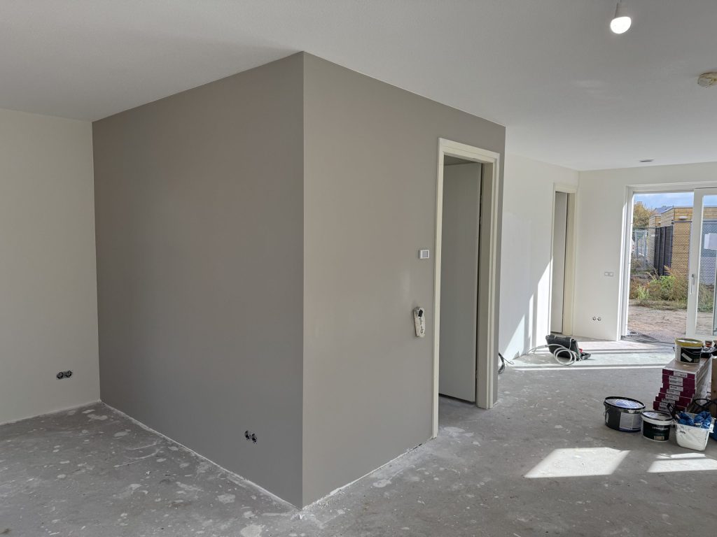 Nieuwe woning met een pas afgewerkte grijze wand, verfemmers op de dekvloer en een tuindeur