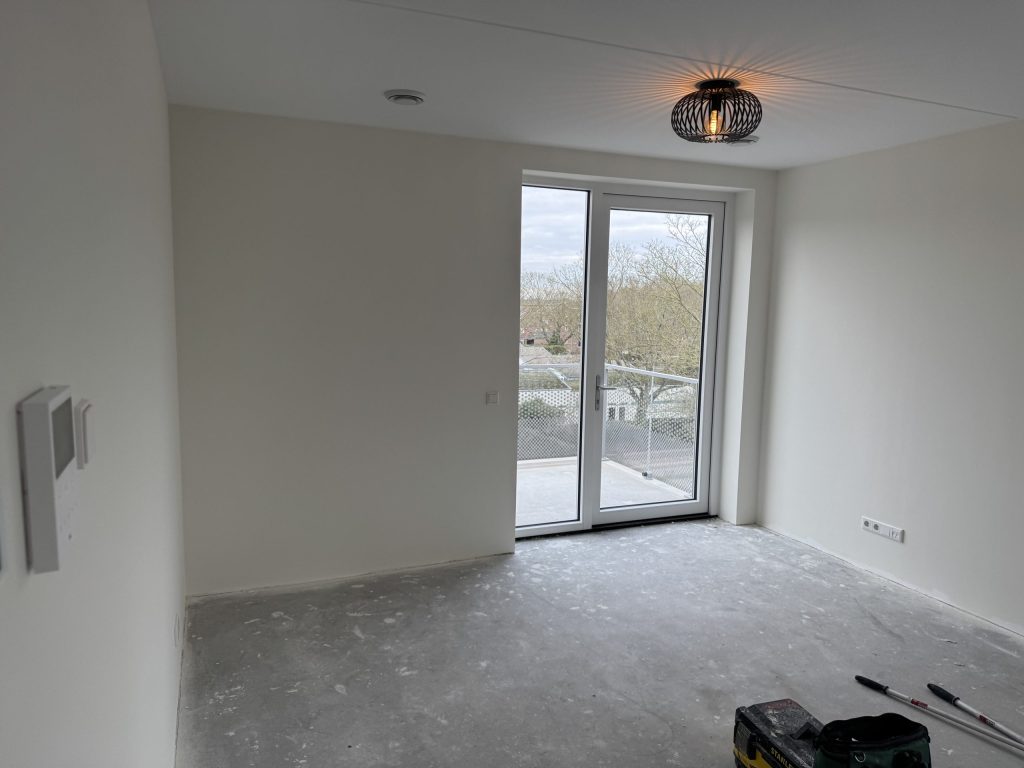 Lege kamer in een nieuw appartement met lichte wanden en een deur naar het balkon
